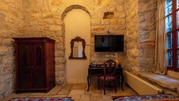 Una habitación con paredes de piedra, un armario de madera, un escritorio con una silla, un televisor y dos camas con ropa de cama estampada.