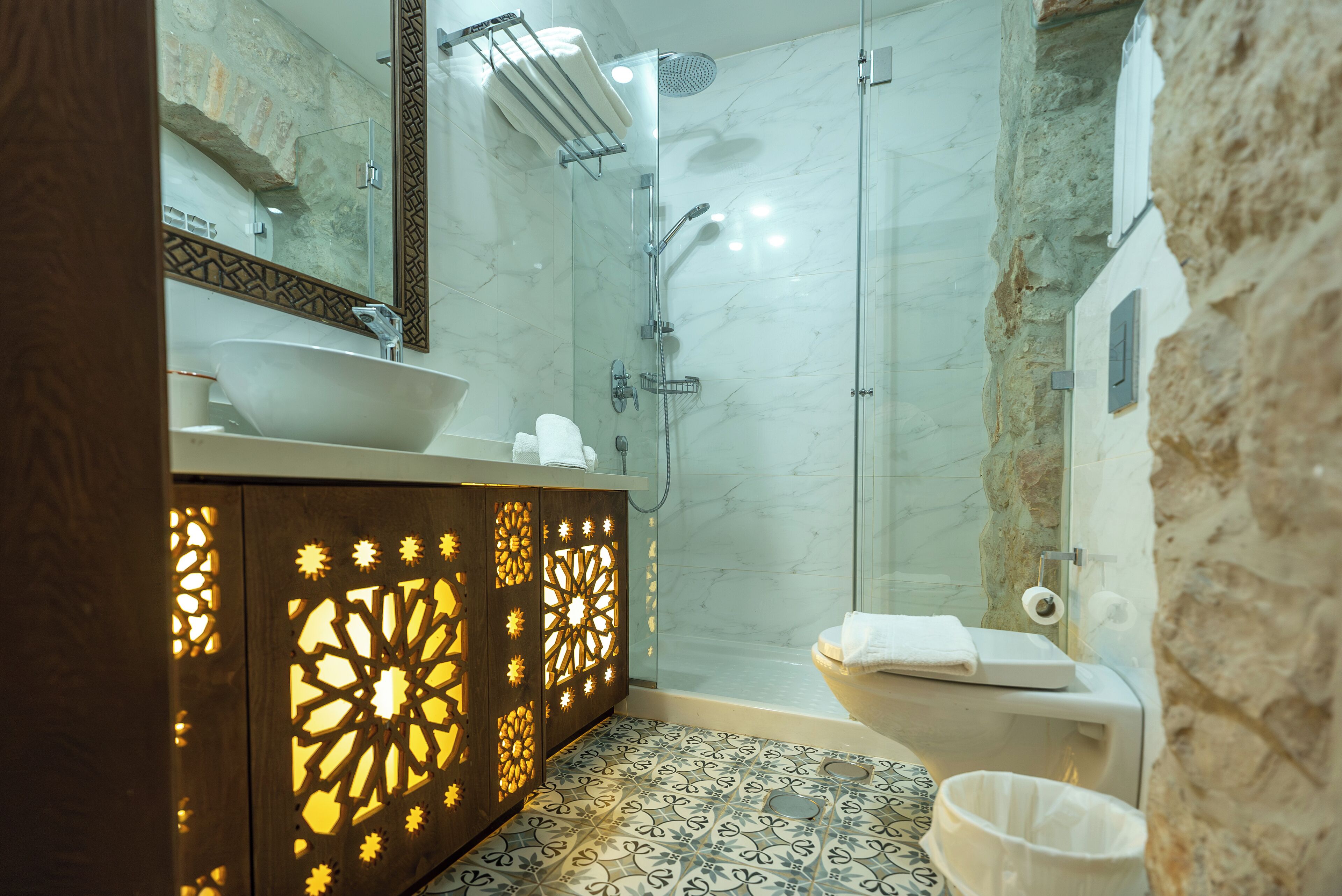 A modern bathroom with a large sink, a glass shower enclosure, and a patterned floor.