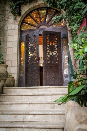 Una escalera de piedra que conduce a una puerta de metal grande y ornamentada, con diseños intrincados y un ventanal de vitrales en la parte superior.