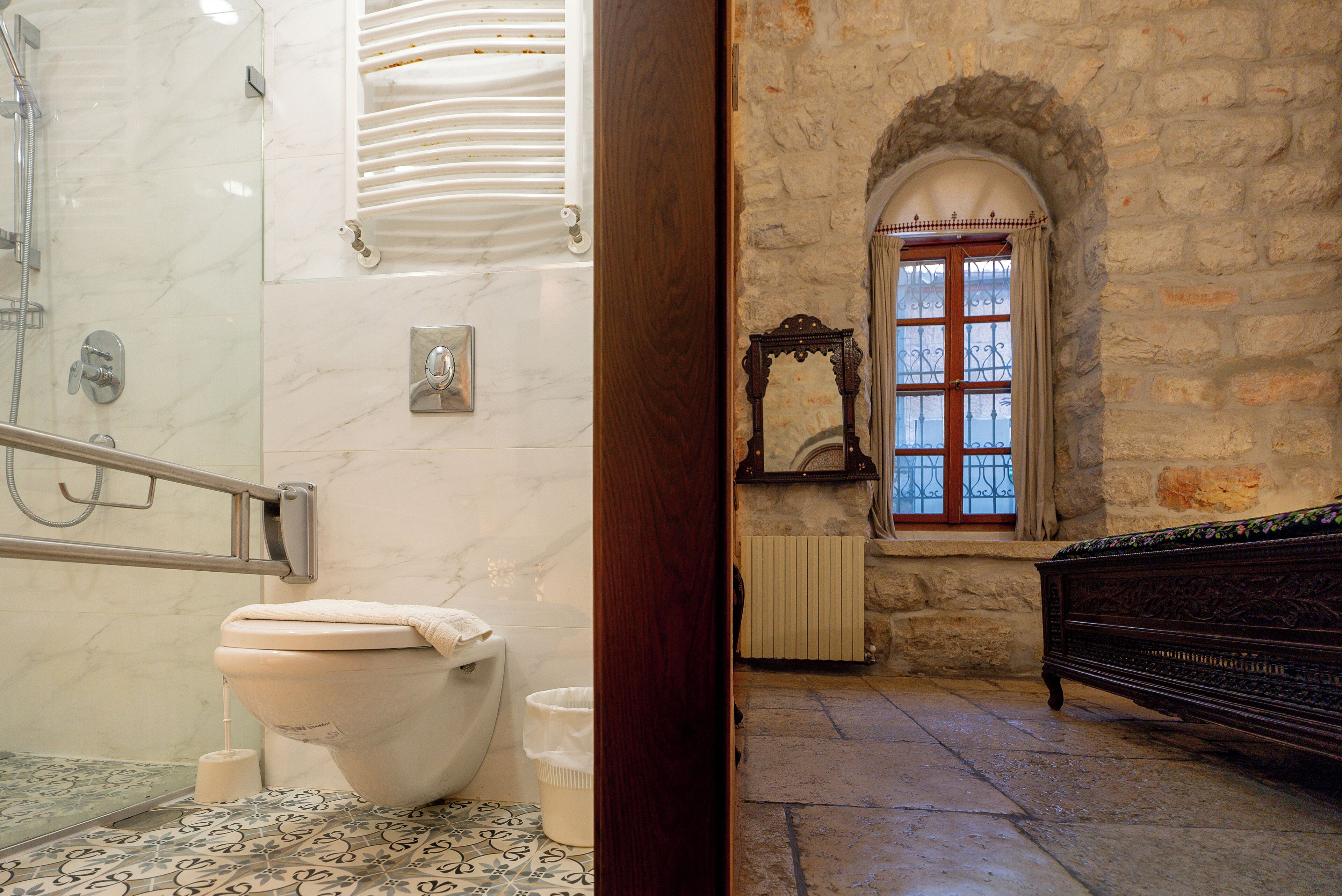 A bathroom with a marble shower, a toilet, and a bench.