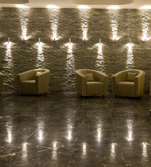A lobby with a stone wall and three beige armchairs. - Main Palace Hotel (Roccalumera)