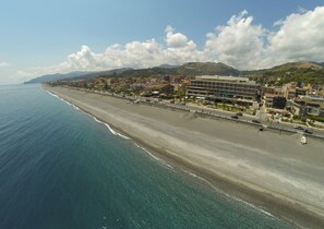 A coastal cityscape with a long beach, buildings, and mountains in the background. - Main Palace Hotel (Roccalumera)