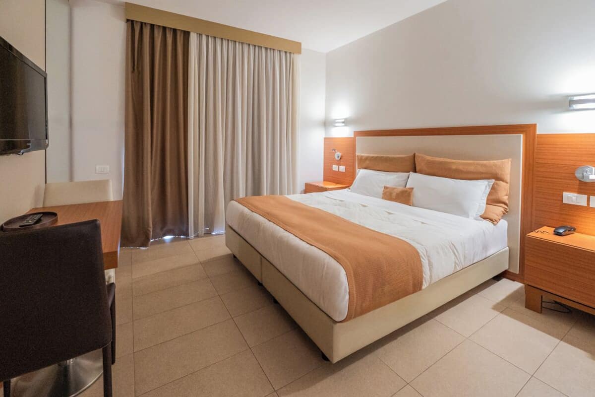 A hotel room with a bed, a desk, a chair, a TV, and a curtain.