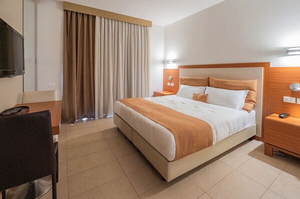 A hotel room with a bed, a desk, a chair, a TV, and a curtain. - Main Palace Hotel (Roccalumera)