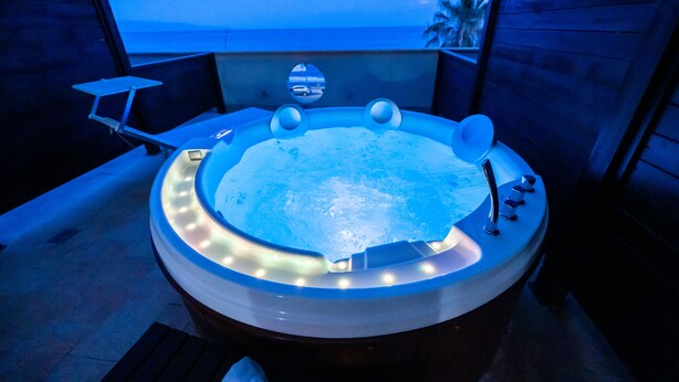 Un bain à remous avec vue sur l’océan, entouré de murs en bois et agrémenté d’une petite table.