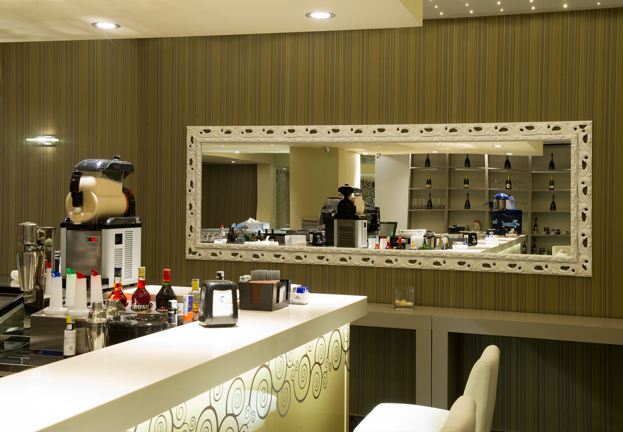 A hotel bar area with a large mirror, bar counter, and shelves of bottles.
