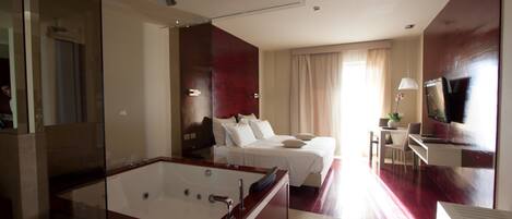 Ein modernes Hotelzimmer mit einer großen Badewanne, einem Bett mit weißer Bettwäsche, einem Schreibtisch mit Stuhl und einem Fernseher.