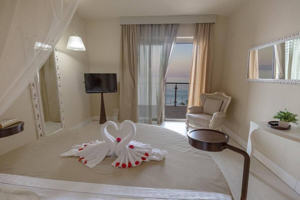 A hotel room with a bed, a TV, a chair, a balcony, and a view of the sea.