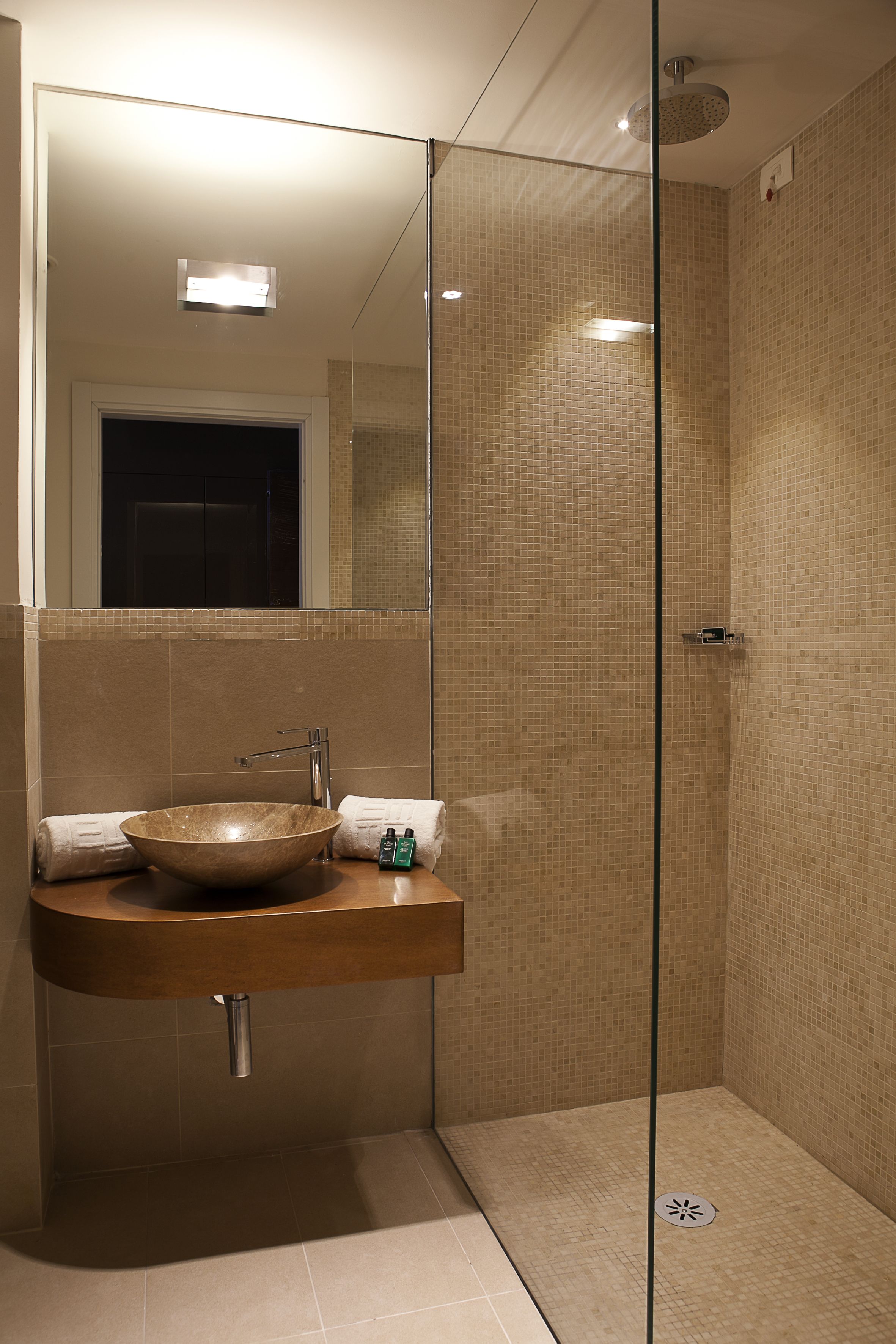 Une salle de bain moderne dotée d’une douche à parois de verre, d’un meuble-lavabo en bois avec un grand lavabo en cuvette et d’un miroir au-dessus du lavabo.