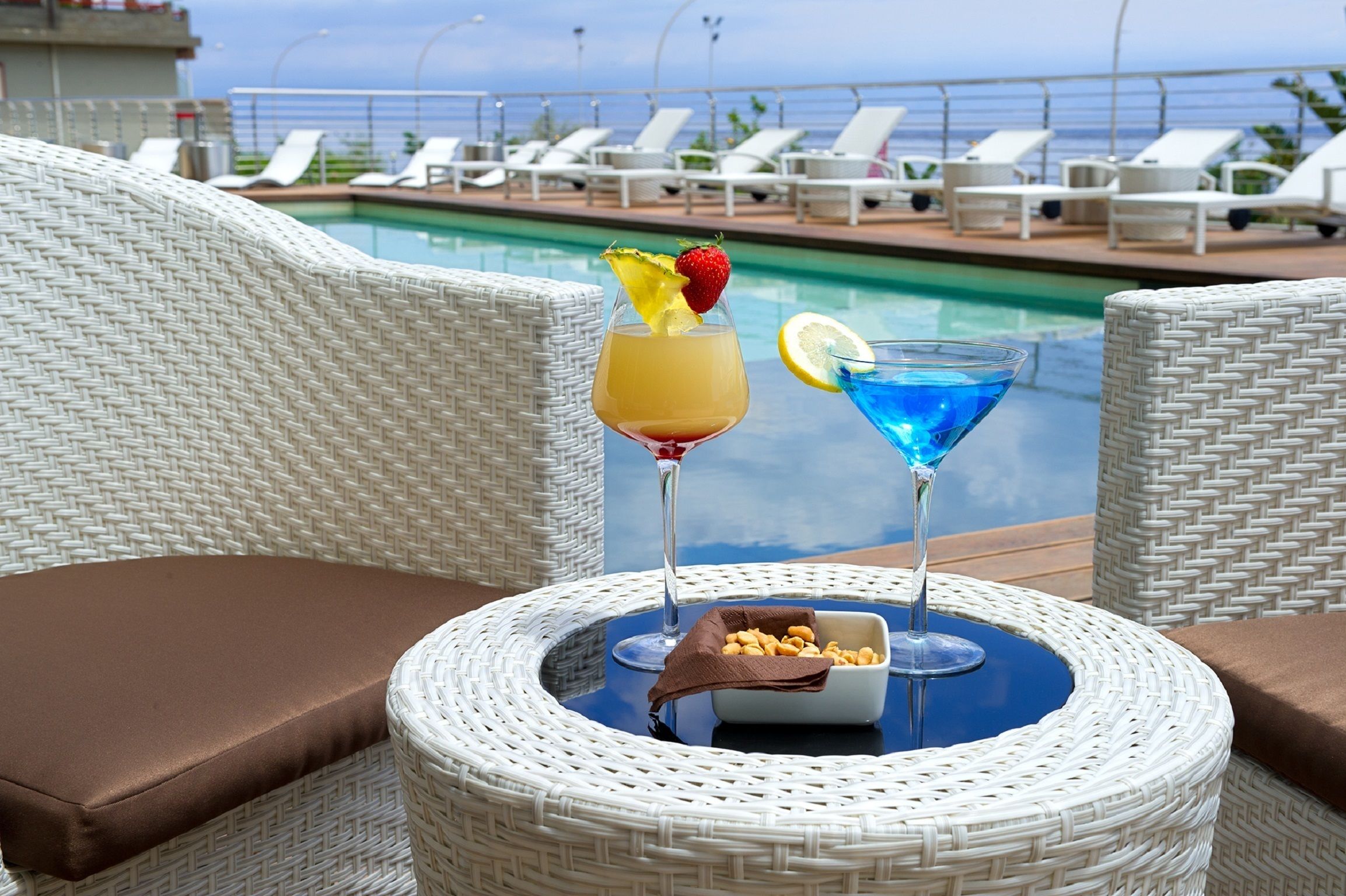 A poolside setting with wicker chairs and a table with drinks and snacks.