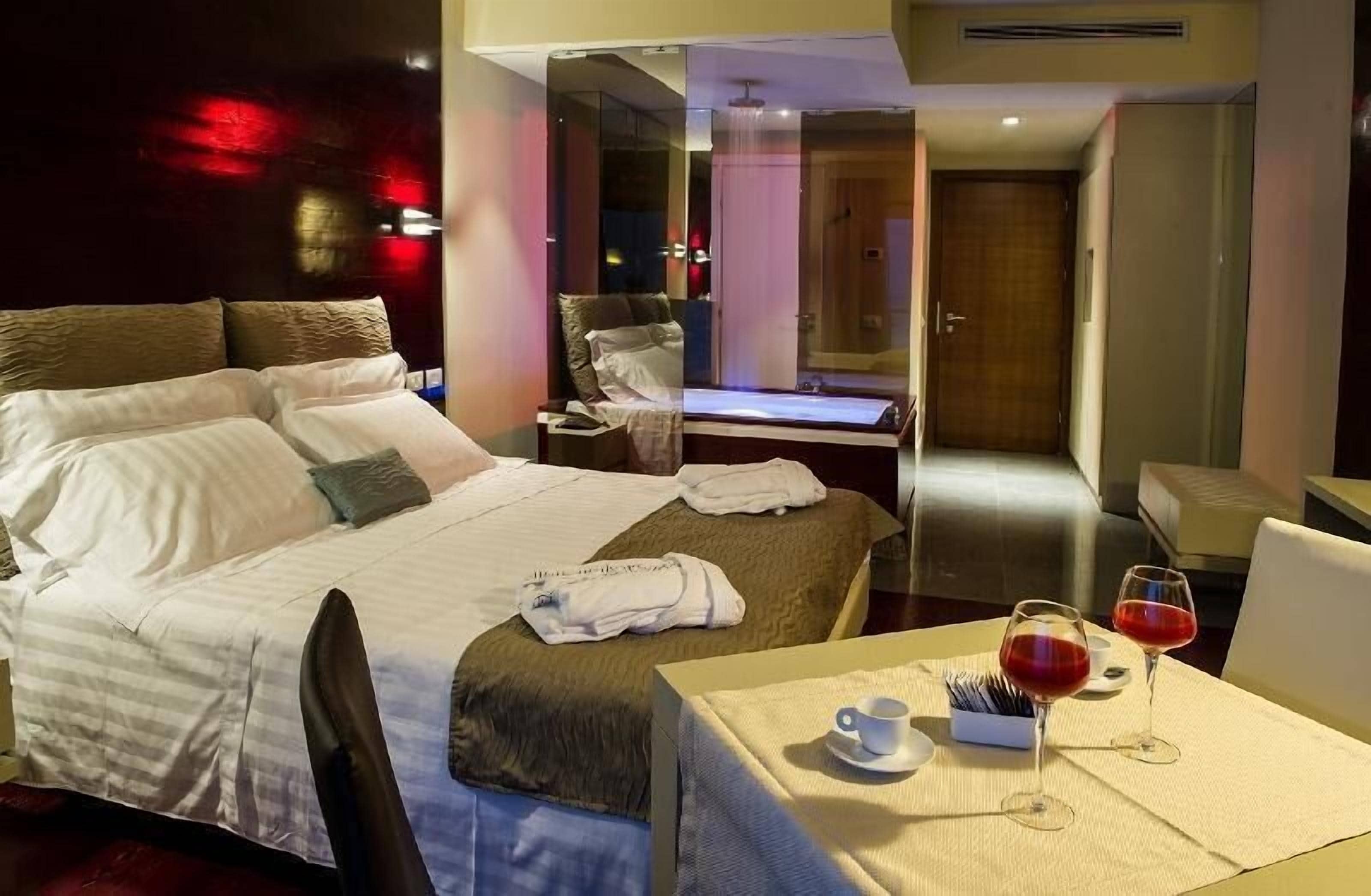 A hotel room with a large bed, a desk, and a table with wine glasses and a cup.