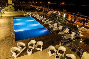 A rooftop pool with lounge chairs and a view of the ocean at night. - Main Palace Hotel (Roccalumera)
