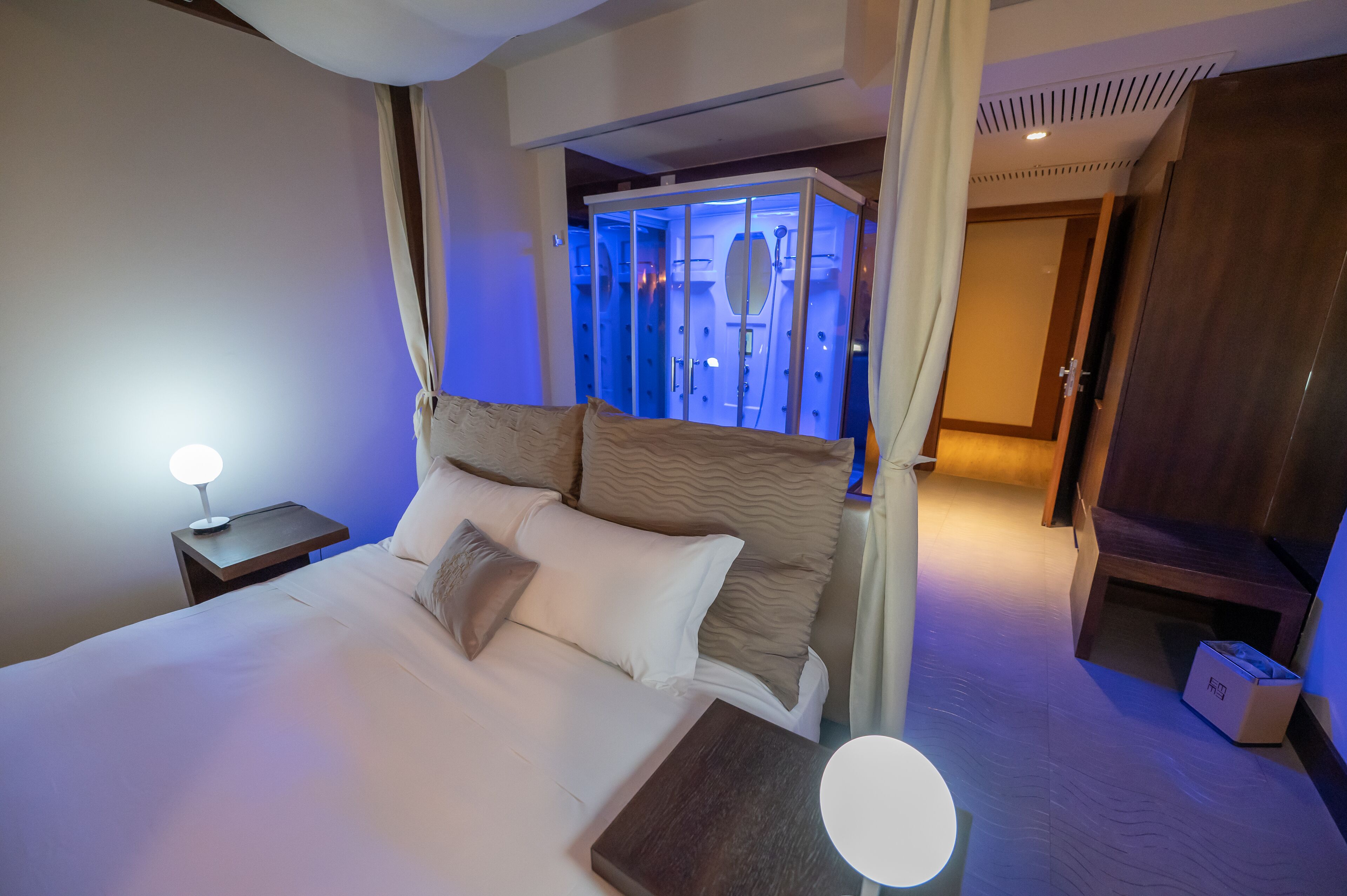 A hotel room with a large bed, a bedside lamp, a wooden nightstand, and a wardrobe.