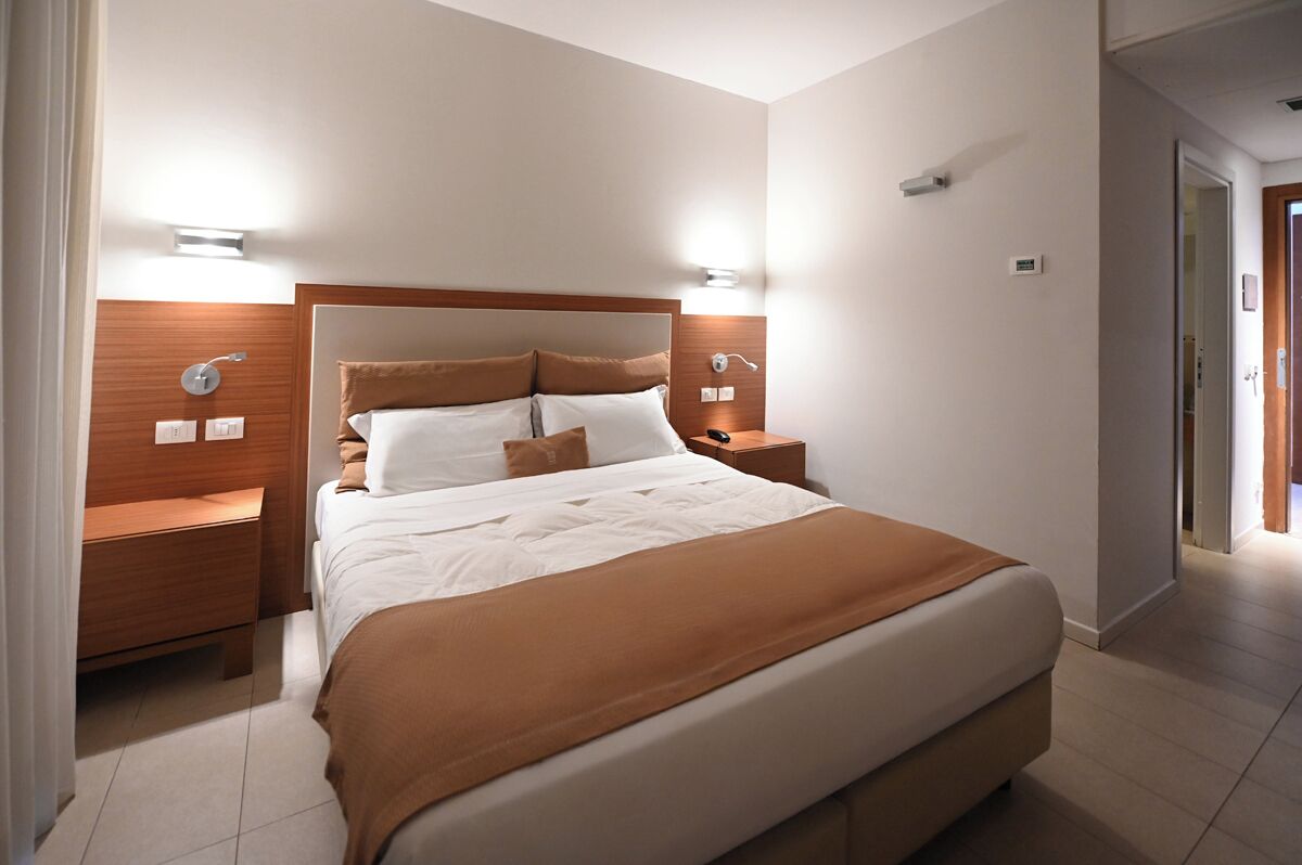 Une chambre d’hôtel avec un grand lit, une tête de lit en bois, des tables de chevet et des lampes fixées au mur.