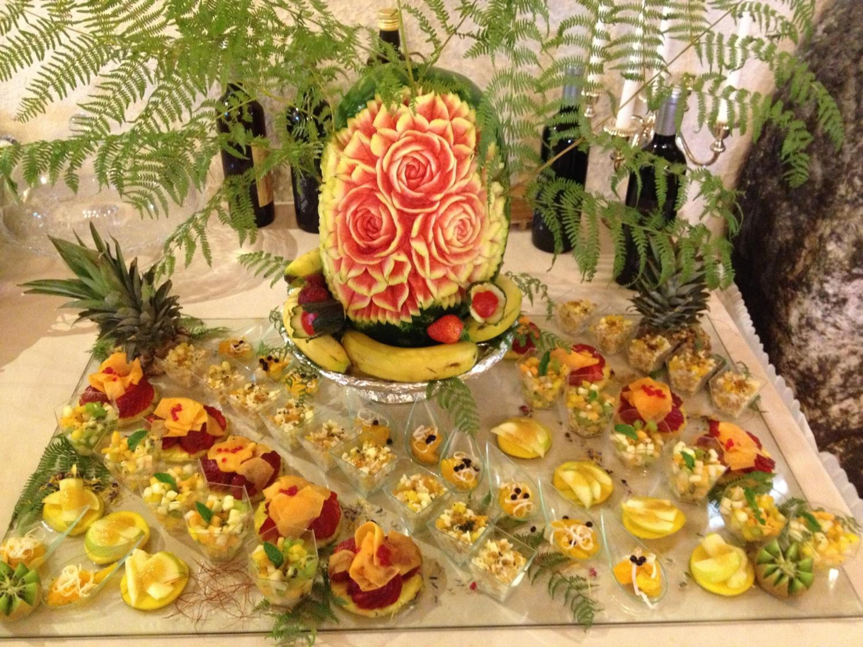 A fruit and vegetable carving display with a central watermelon rose and various fruit arrangements.