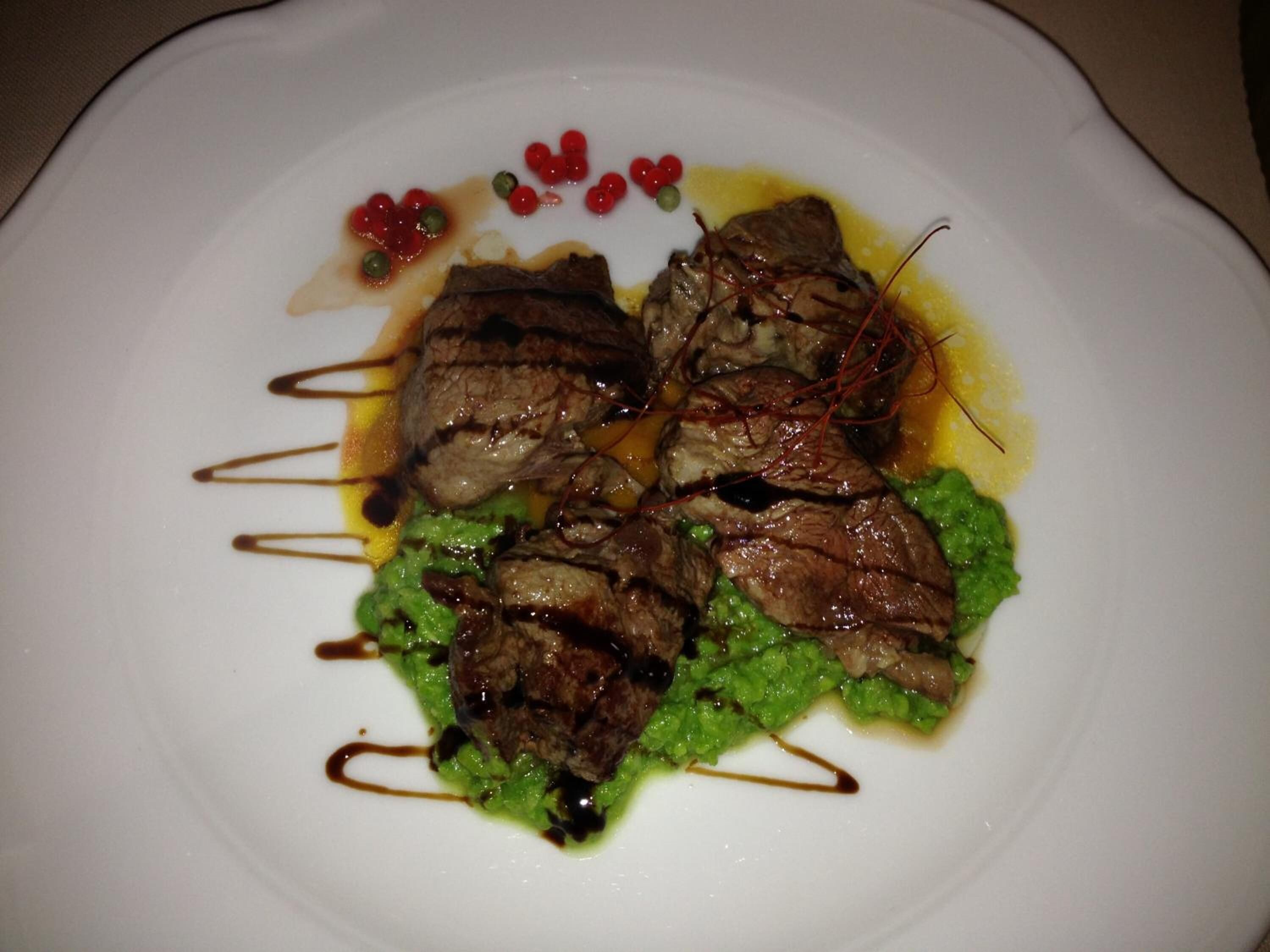 A plate of food with meat and green sauce, garnished with red berries and a drizzle of sauce.