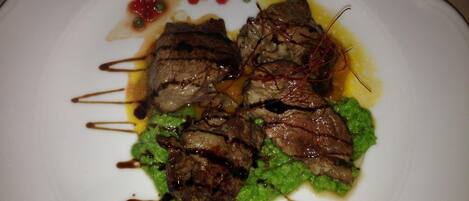 A plate of food with meat and green sauce, garnished with red berries and a drizzle of sauce.