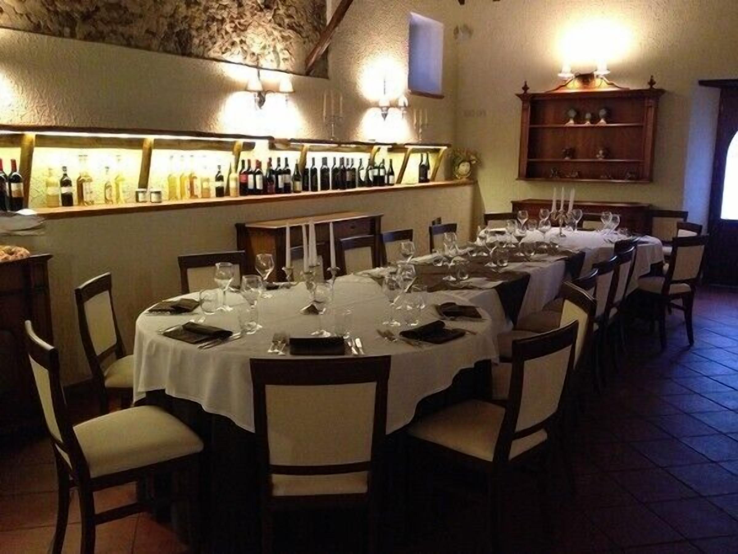 Een restaurant met ronde tafels gedekt voor diners, een wijnrek met flessen en een stenen muur.