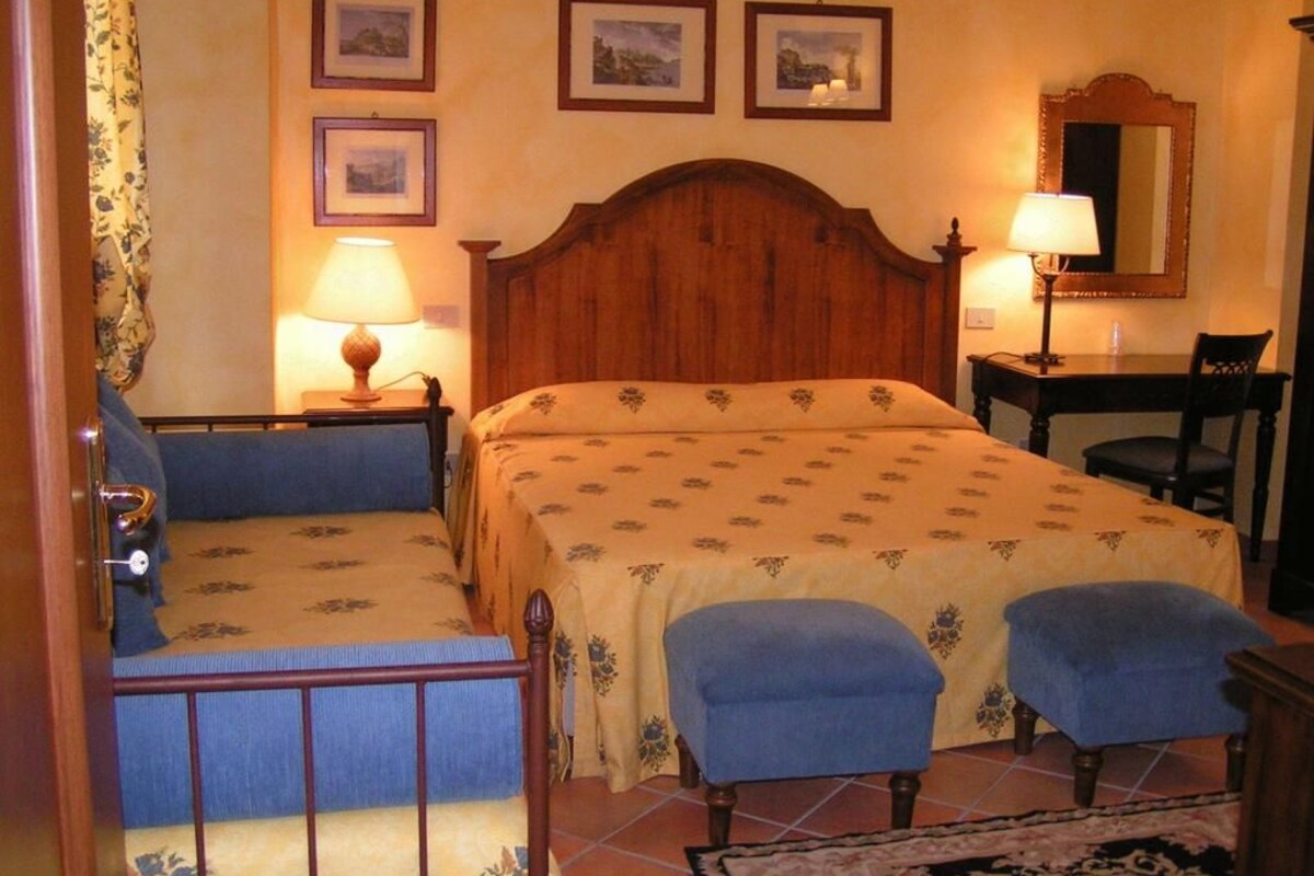 Um quarto com uma cama de madeira, duas luminárias de cabeceira, uma cadeira, uma escrivaninha e um espelho.