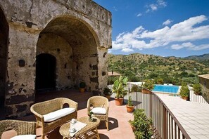A terrace with wicker furniture, a stone archway, and a pool in the background. - Il Borgo Country Resort (Castiglione di Sicilia)