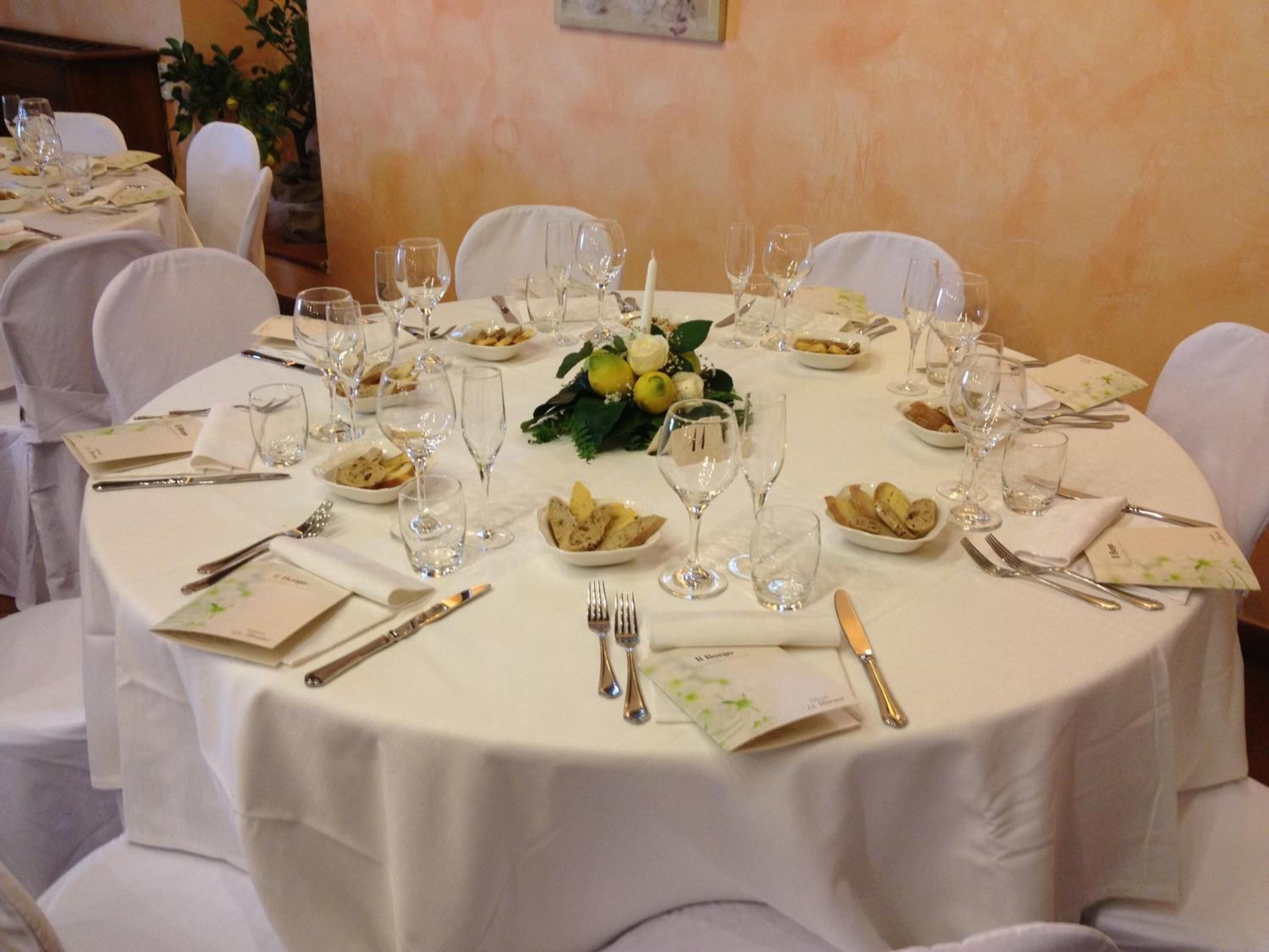 A round dining table set for a formal meal with white tablecloths, glassware, and neatly arranged plates and cutlery.
