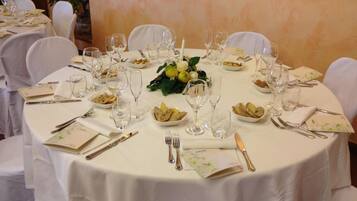 Une table ronde dressée pour un repas formel, avec des nappes blanches, de la verrerie et des assiettes et couverts disposés avec soin.