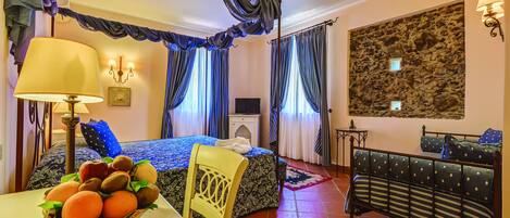 Une chambre d’hôtel avec un lit, un canapé, une table à manger avec des fruits, des rideaux et un mur en pierre.