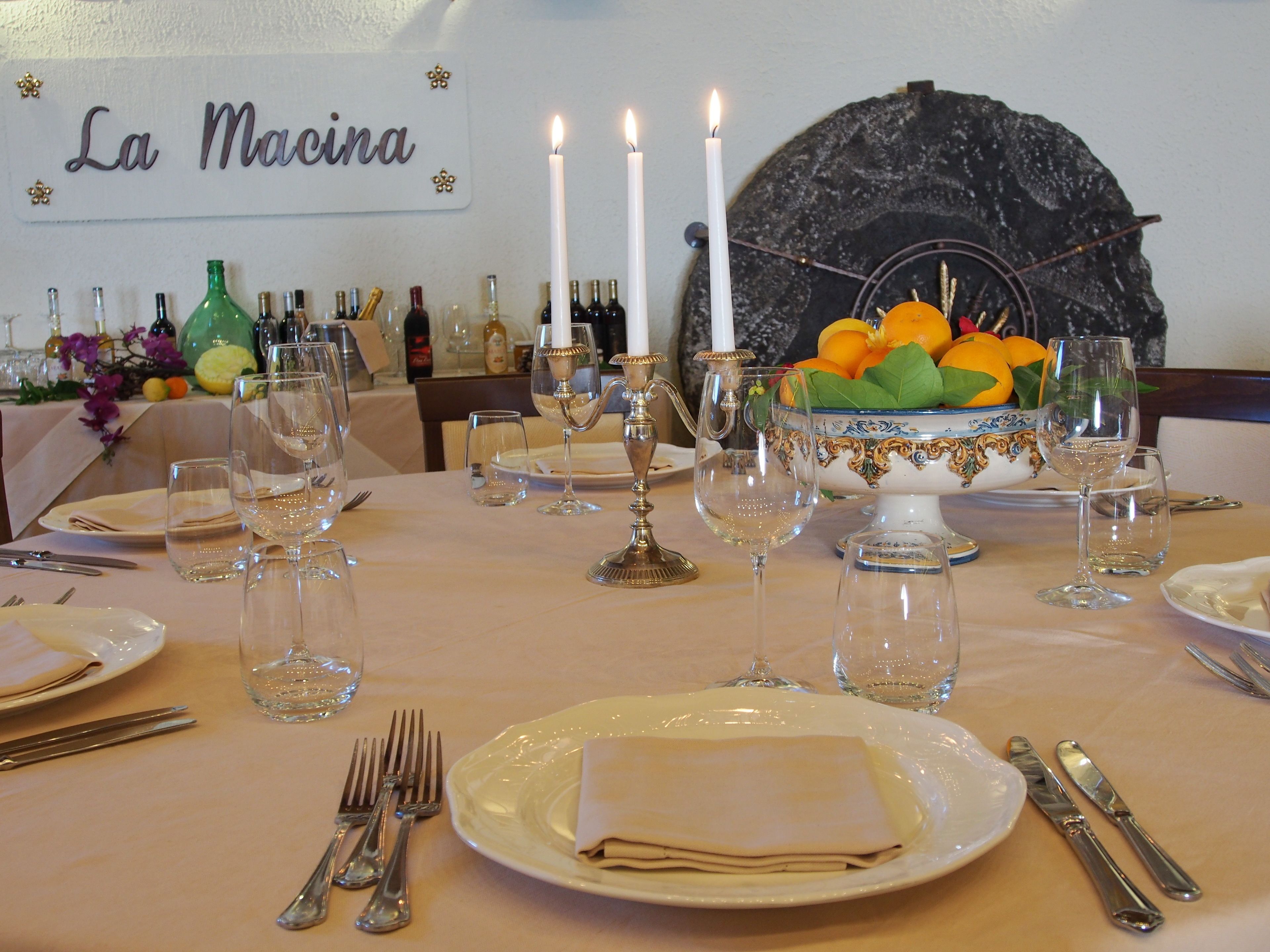 A dining table set with plates, cutlery, wine glasses, and a centerpiece with fruit and candles.