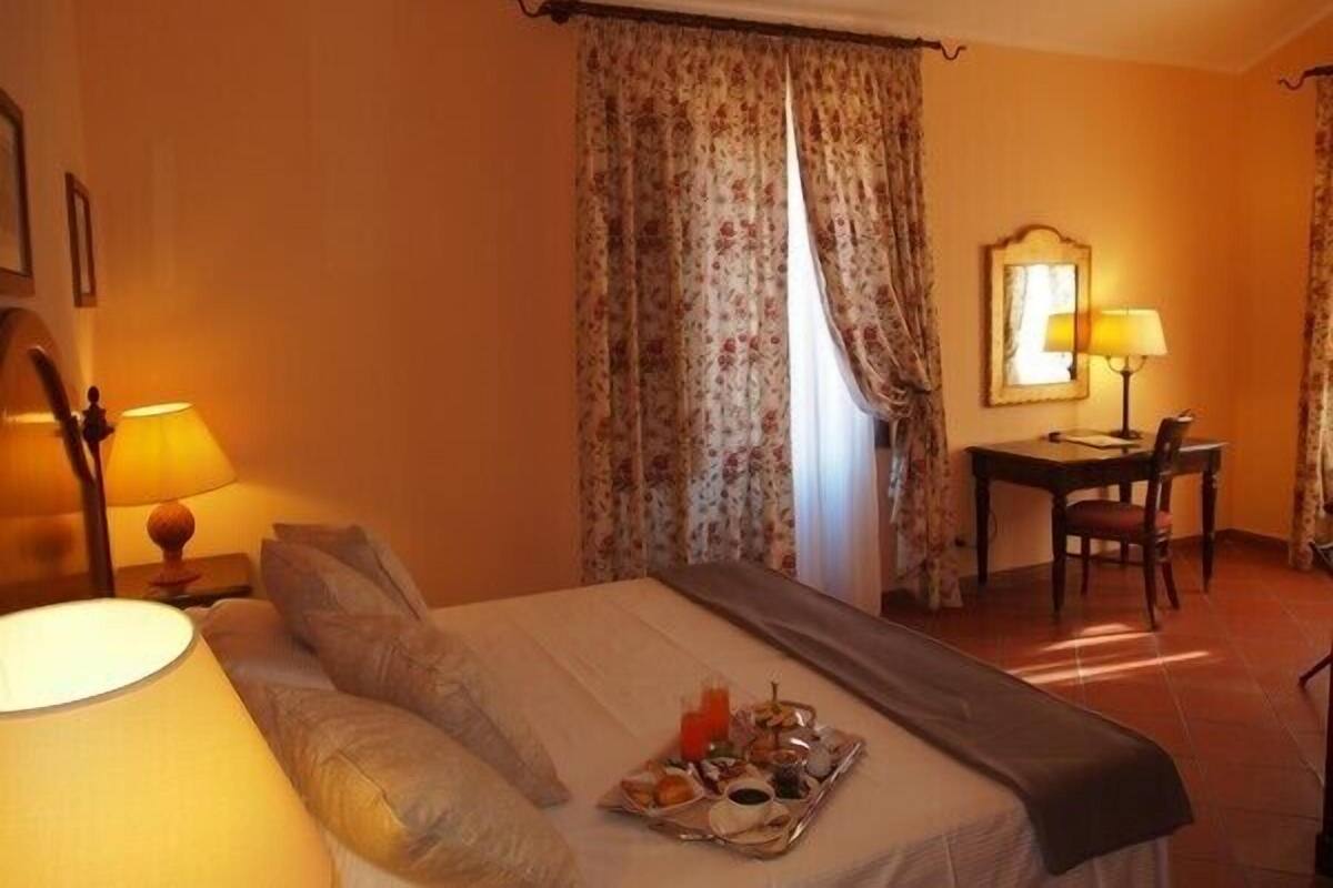 A hotel room with a bed, a desk, a chair, and a tray of breakfast items.