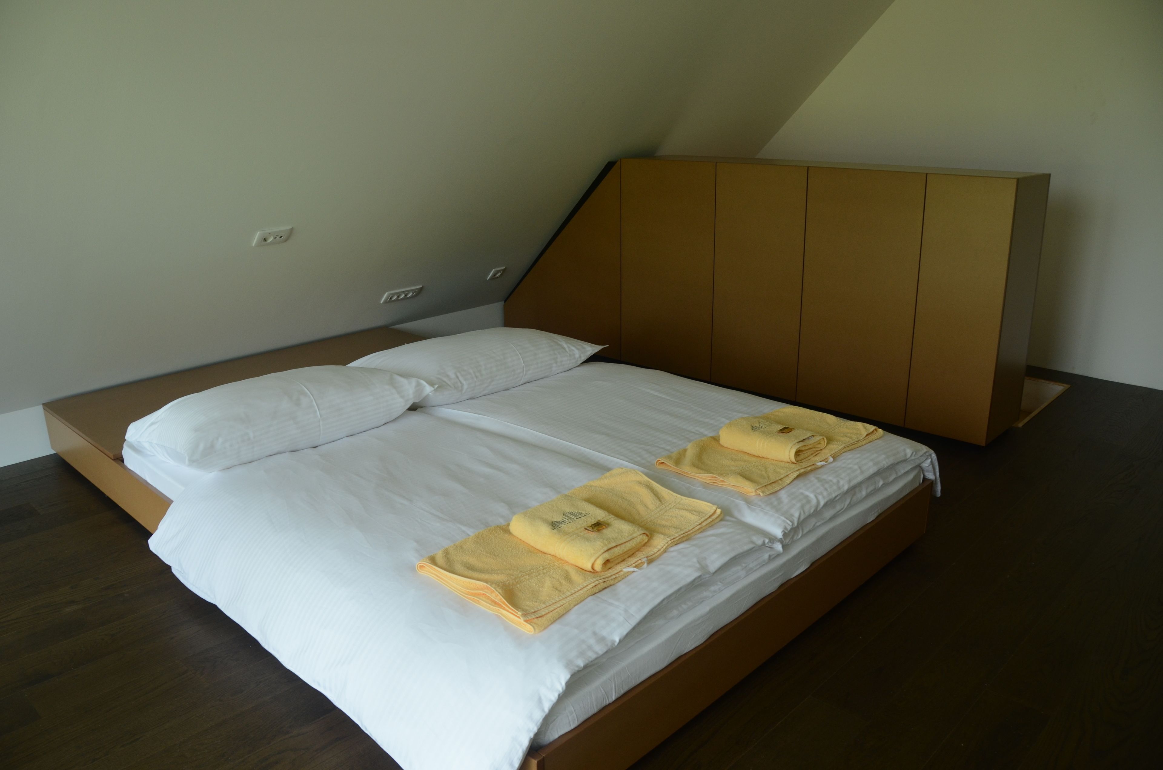 A bed with white linens and two yellow towels, a wooden headboard, and a sloped ceiling.