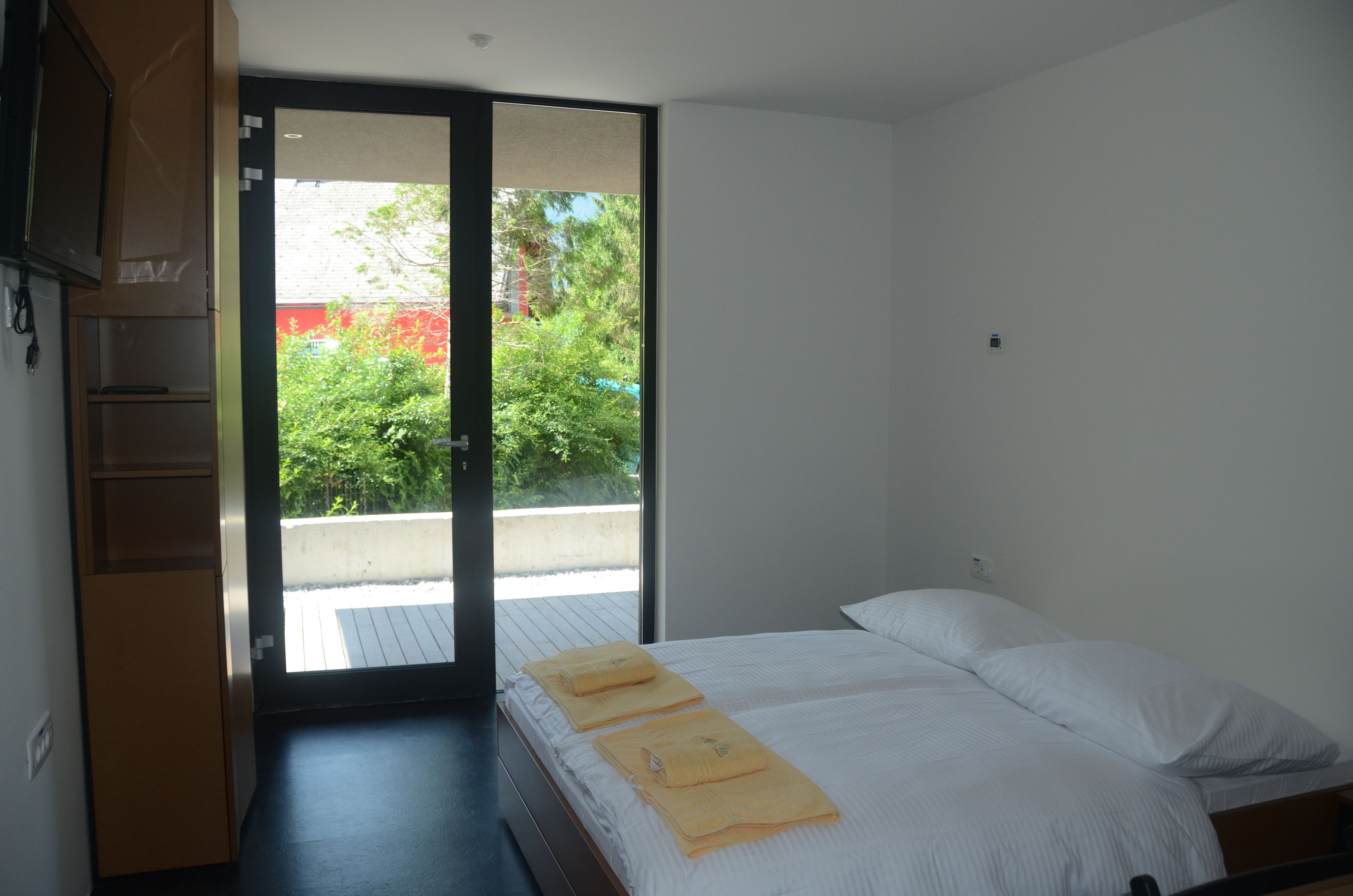 Ein Schlafzimmer mit einem Bett, einer Schiebetür zu einem Außenbereich und einer kleinen Regaleinheit.