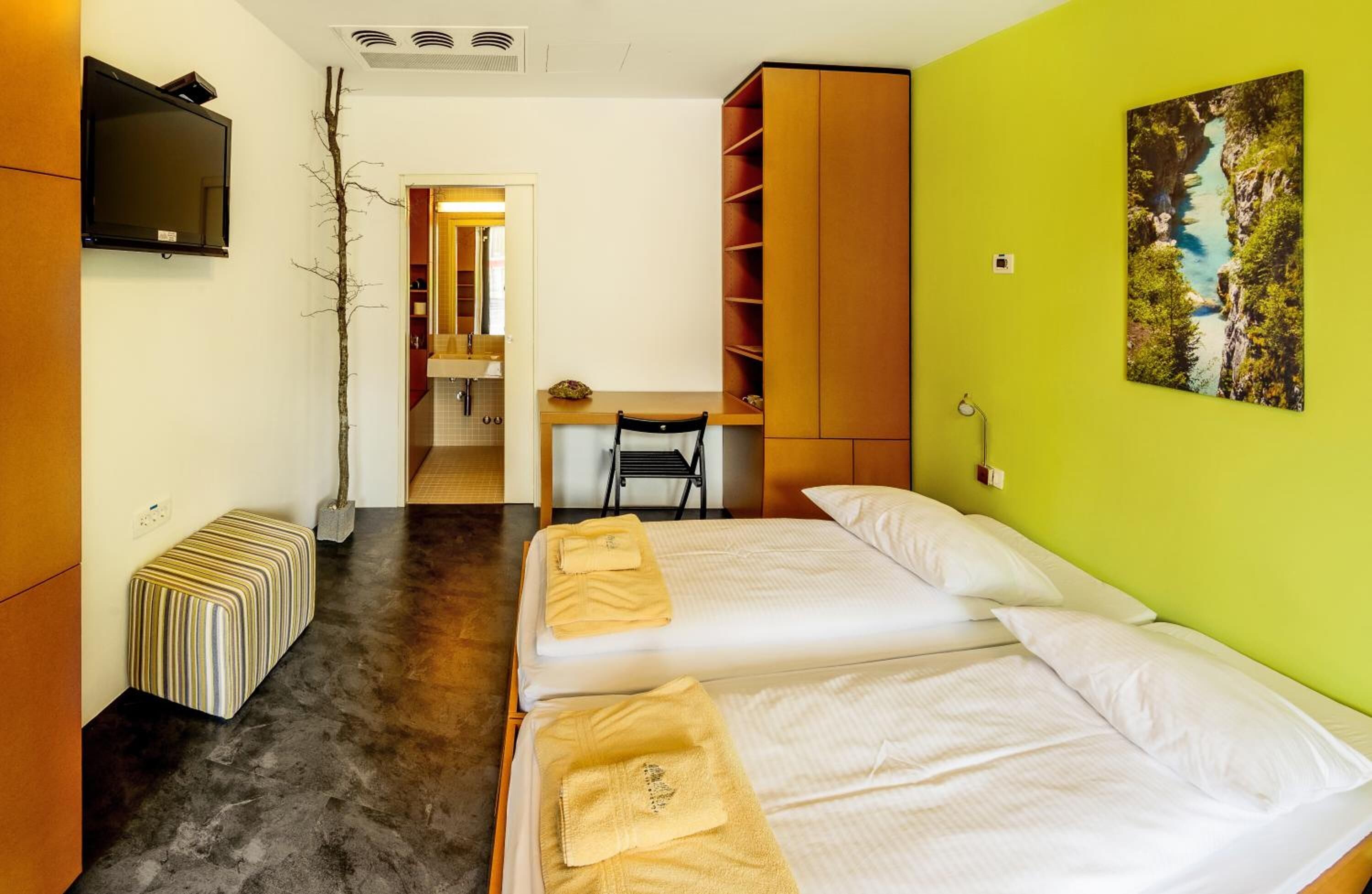 A hotel room with two beds, a desk, a TV, and a painting on the wall.