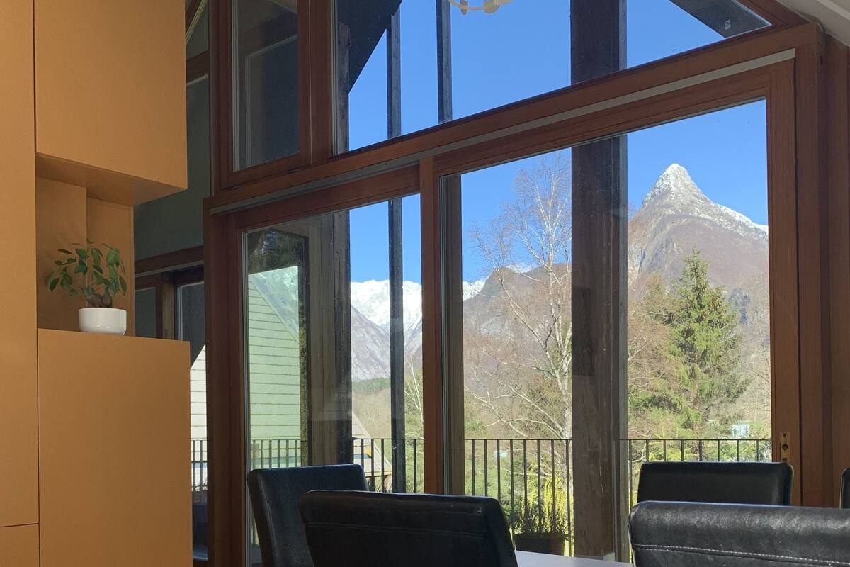 Un espace repas comprenant une table et des chaises, de grandes fenêtres offrant une vue sur les montagnes et un luminaire suspendu.