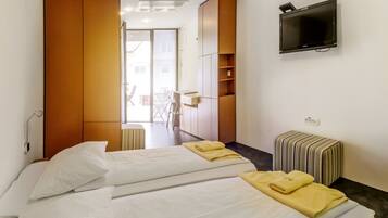 A hotel room with two beds, a TV, a small table, and a view of the outside.