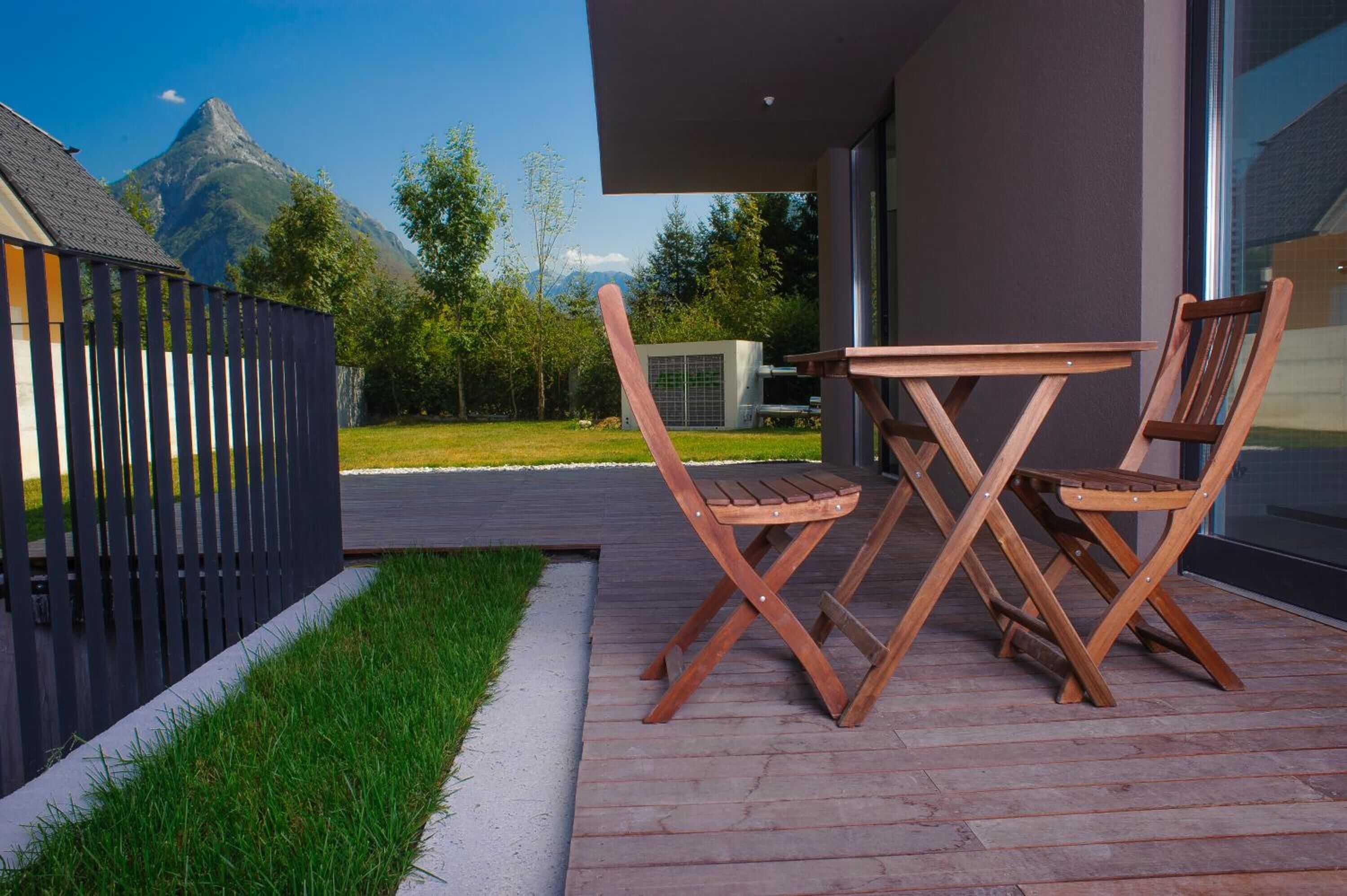 Eine moderne Außenpatio mit einem Holztisch und -stühlen, einem schwarzen Zaun und Blick auf die Berge.