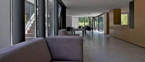 A modern interior with a long corridor, large windows, and a seating area with a staircase visible outside.