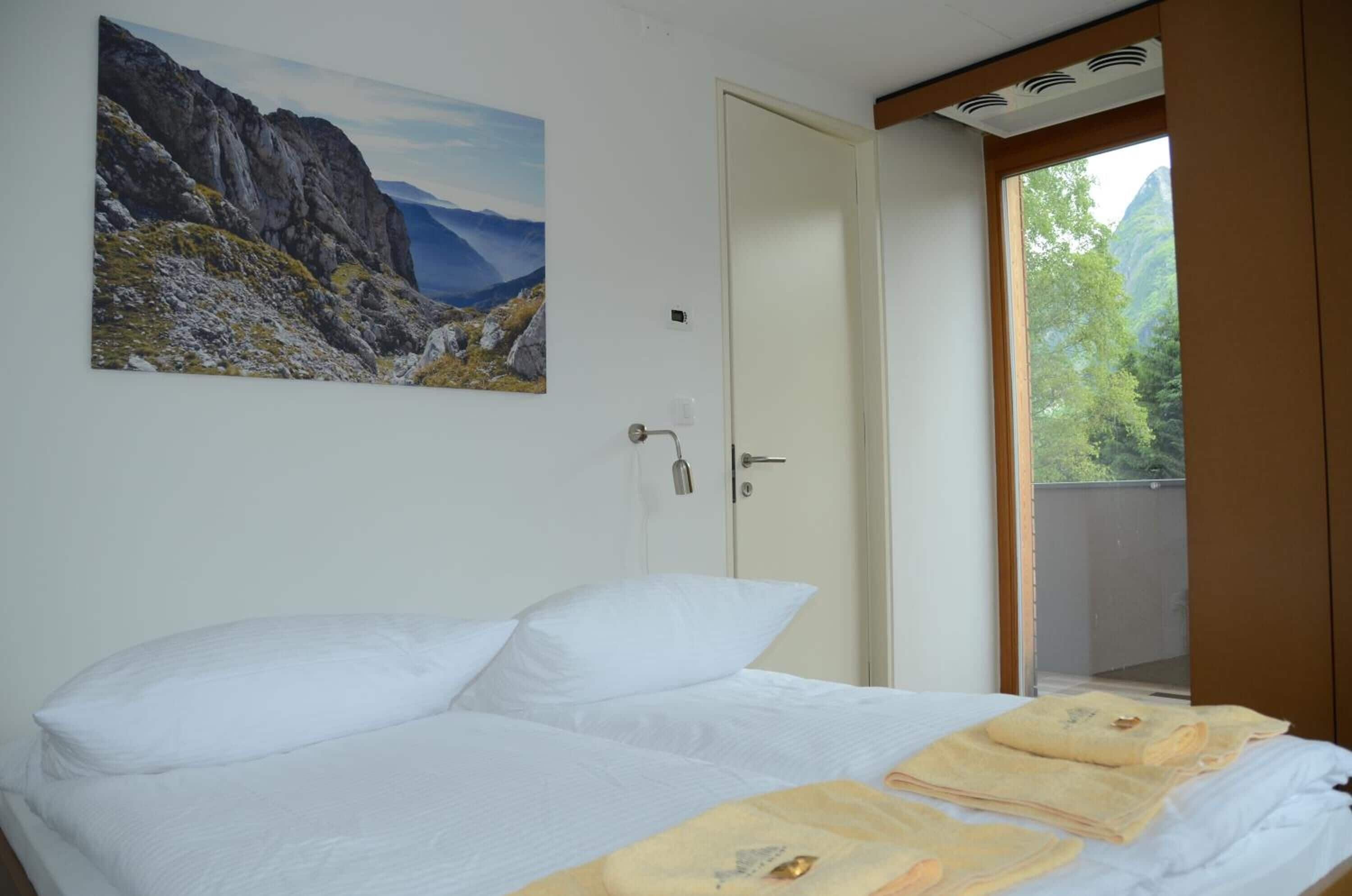 A bedroom with a bed, a door, a window, and a painting on the wall.