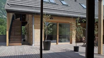 A modern wooden house with a wooden deck, a staircase leading to an upper level, and potted plants.