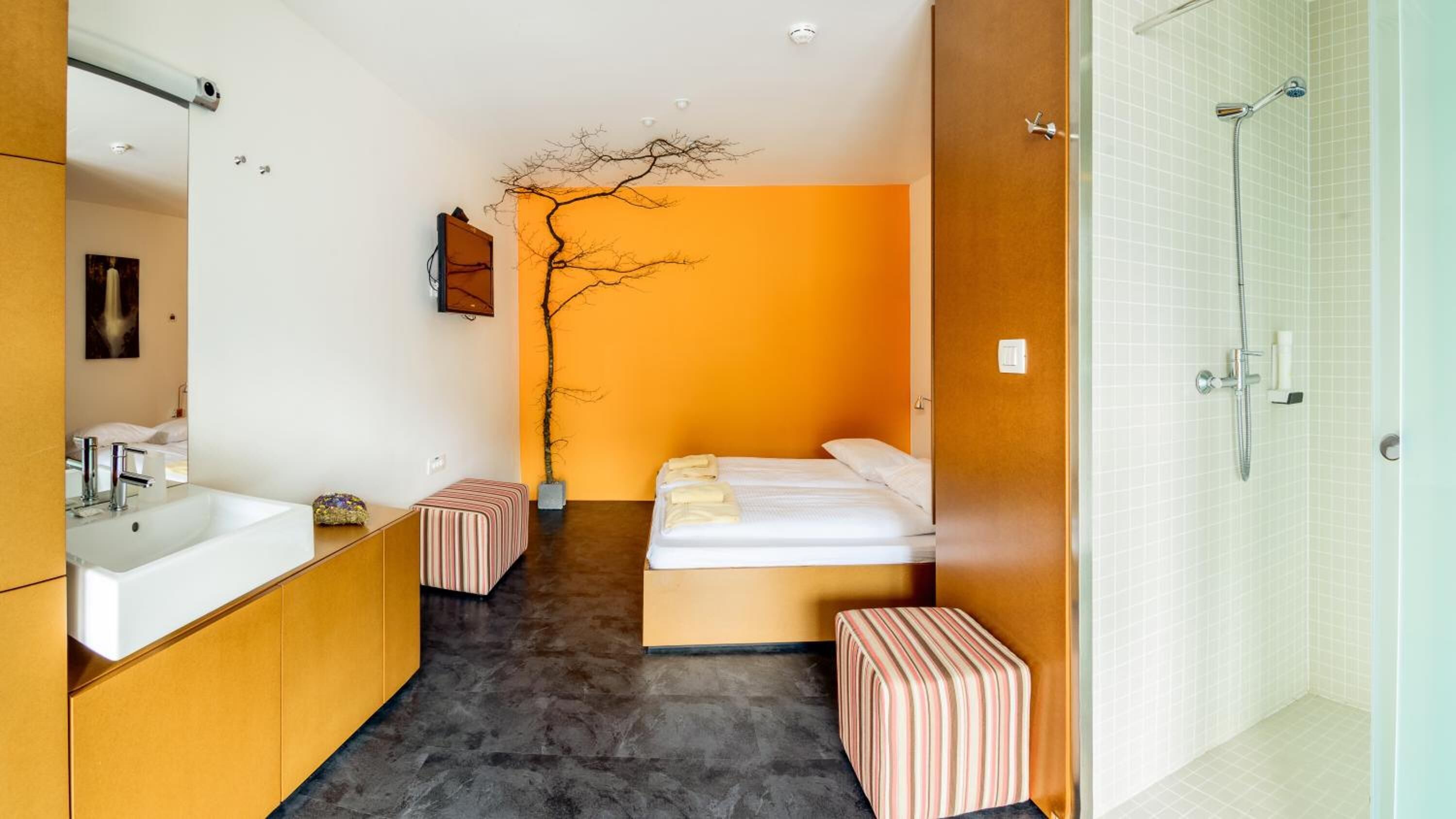 Ein modernes Hotelzimmer mit einem großen Bett, einem kleinen Nachttisch, einem Badezimmer mit Dusche und einem großen Spiegel.