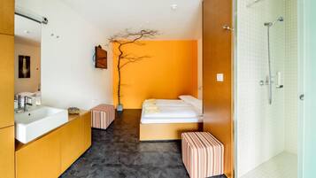 Ein modernes Hotelzimmer mit einem großen Bett, einem kleinen Nachttisch, einem Badezimmer mit Dusche und einem großen Spiegel.