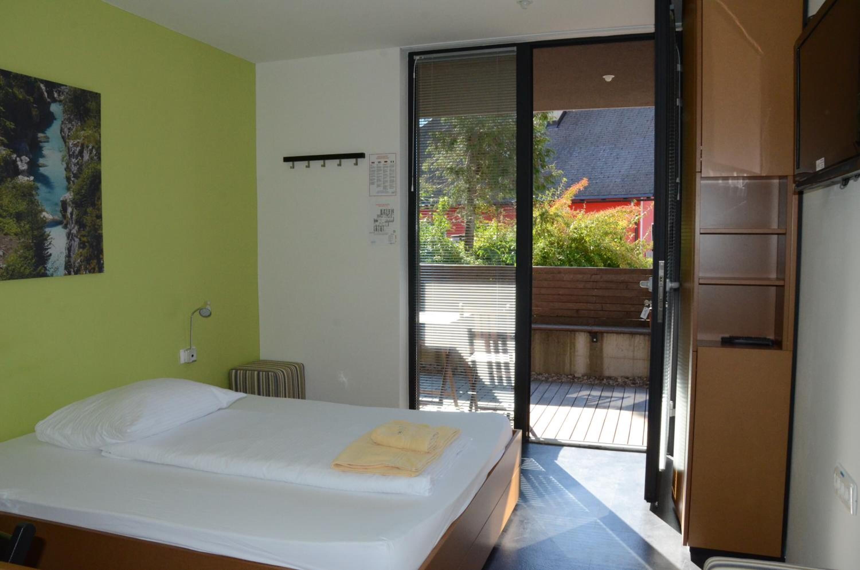 A hotel room with a bed, a window with blinds, a radiator, and a view of the outside.