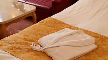 A neatly made bed with a folded white towel, a patterned yellow and white bedspread, and a red leather chair in the background.