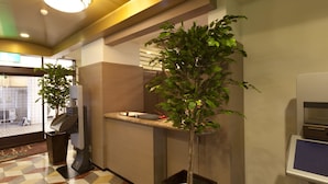 A reception area with a check-in counter, a digital kiosk, and two potted plants.