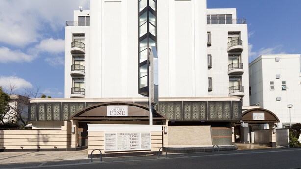 A modern hotel with a prominent entrance, multiple balconies, and a clear sky.