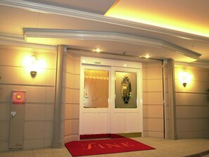 A hotel entrance with a red carpet, a glass door with a decorative frame, and wall-mounted lights.