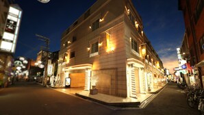 A multi-story hotel with a modern facade, illuminated by warm lighting, located on a busy street with visible signage and parked bicycles. - Fine Garden Umeda (Osaka)