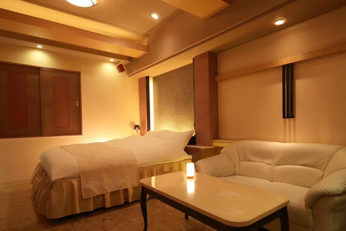 A room with two beds, a sofa, a table, and a lamp.