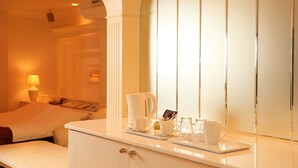A hotel room with a bed, a bedside table with a lamp, a coffee maker, and a tray with cups and a small cake. - Fine Garden Umeda (Osaka)