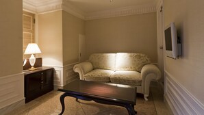 A living room with a glass-top coffee table, a sofa, a lamp, and a television mounted on the wall. - Hotel Fine Aroma Dotonbori (Osaka)