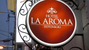 A circular sign with the text "HOTEL LA AROMA DOTTONBORI" and a decorative fleur-de-lis symbol above the text. - Hotel Fine Aroma Dotonbori (Osaka)